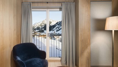 Stuhl und Lampe neben Fenster mit Blick auf verschneite Berge und Dorf