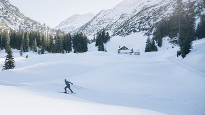 Langläufer in winterlicher Berglandschaft mit Schneehütte und Tannen
