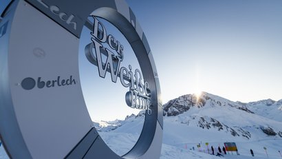 Schild Der Weiße Ring mit schneebedeckten Bergen und Sonne im Hintergrund