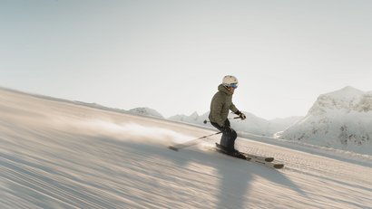Skifahrer fährt auf verschneiter Piste in den Bergen bei Sonnenlicht