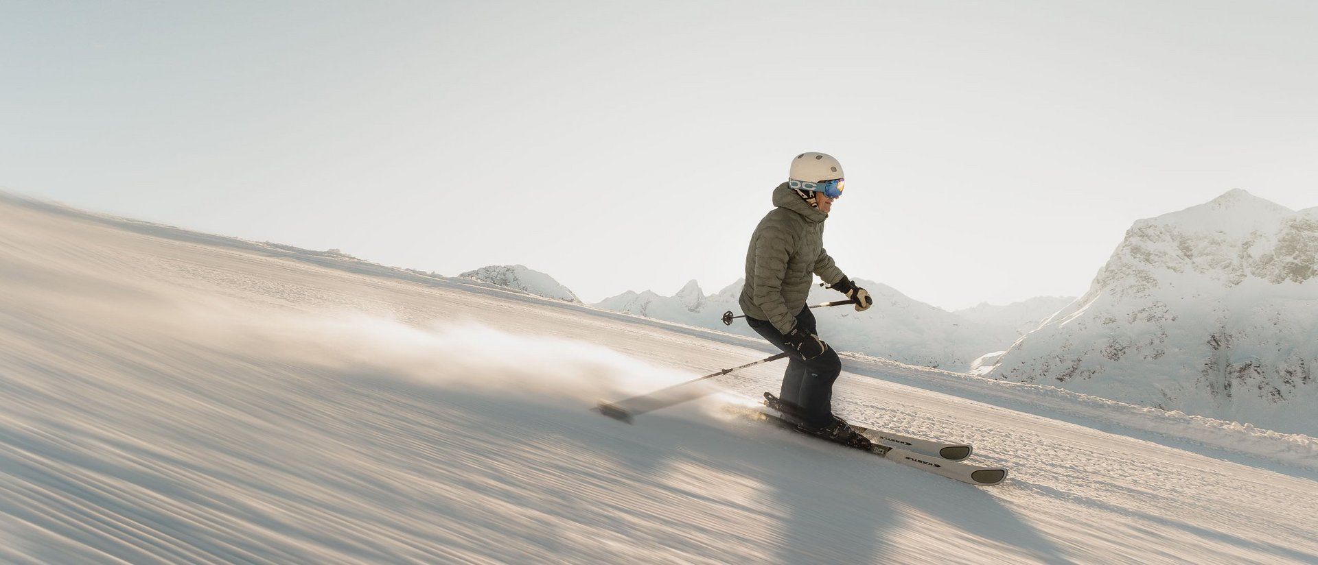 Skifahrer fährt auf verschneiter Piste in den Bergen bei Sonnenlicht