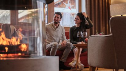Paar sitzt gemütlich am Kamin mit zwei Gläsern Rotwein im Wohnzimmer.