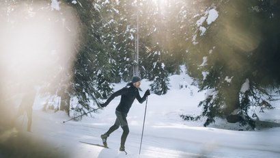 Mann beim Langlaufen in verschneitem Wald bei Sonnenlicht