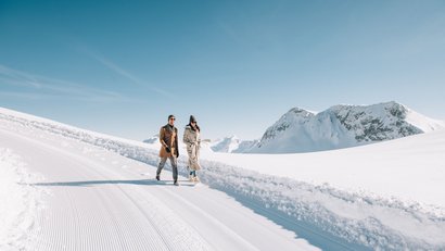 Paar spaziert auf verschneitem Weg mit gebirgiger Winterlandschaft