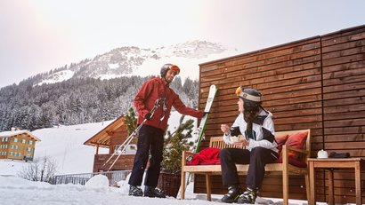 Zwei Skifahrer machen Pause vor einer Holzhütte im verschneiten Berggebiet