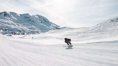Skifahrer fährt auf einer verschneiten Piste in den Bergen bei sonnigem Wetter