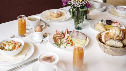 Frühstückstisch mit Aufschnitt, Eiern, Brötchen, Saft und Kaffee