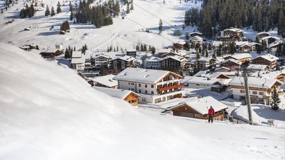 Skifahrer in verschneitem Bergdorf mit Holzhäusern und Tannenbäumen