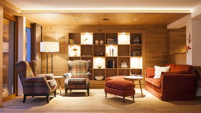 Gemütliches Wohnzimmer mit zwei Sesseln, Sofa und beleuchtetem Regal aus Holz