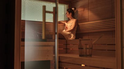 Frau in Handtuch entspannt in hölzerner Sauna mit Holzeimer