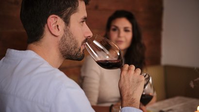 Mann riecht an Rotweinglas, Frau im Hintergrund an einem gedeckten Tisch