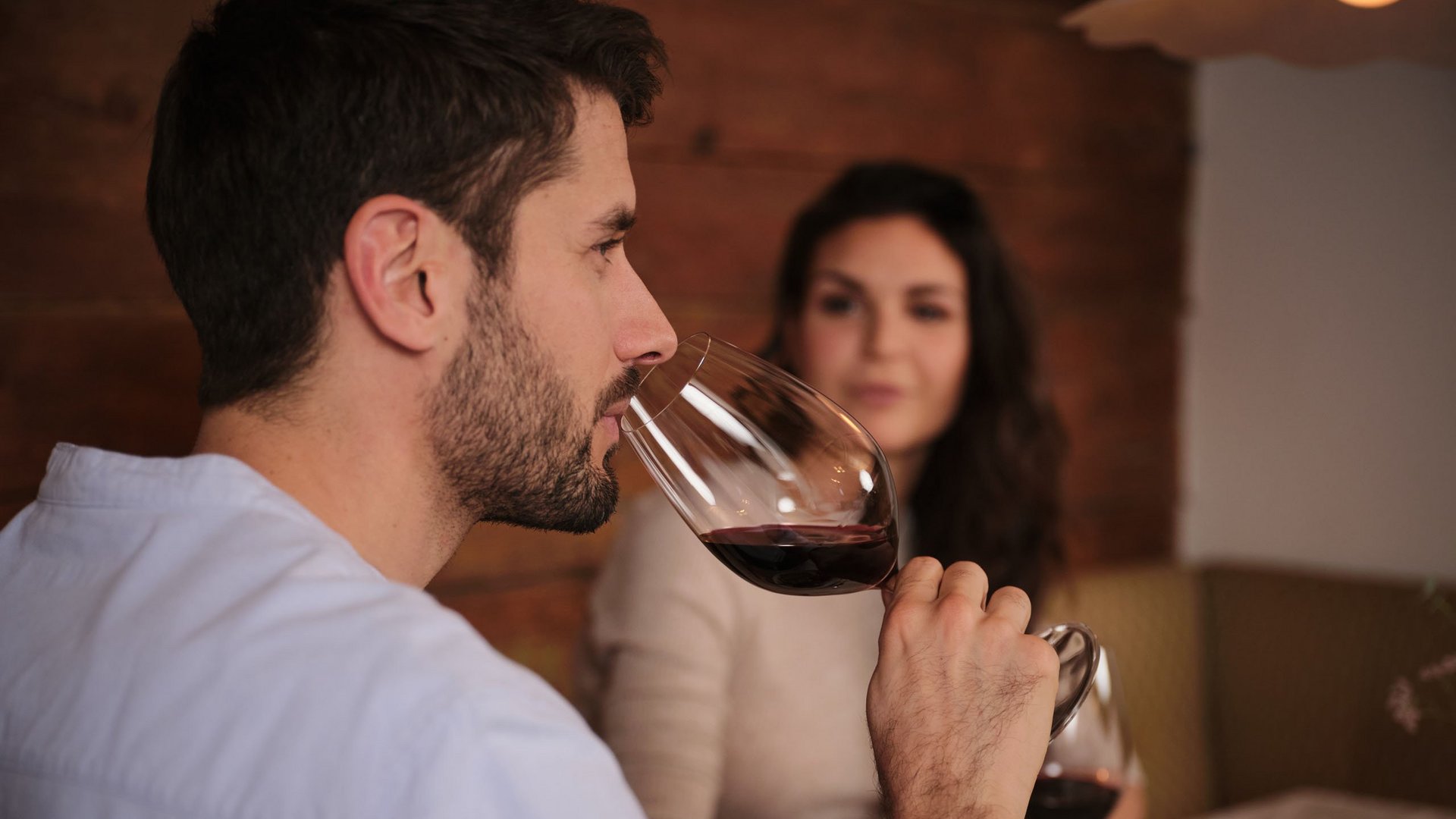Mann riecht an Rotweinglas, Frau im Hintergrund an einem gedeckten Tisch